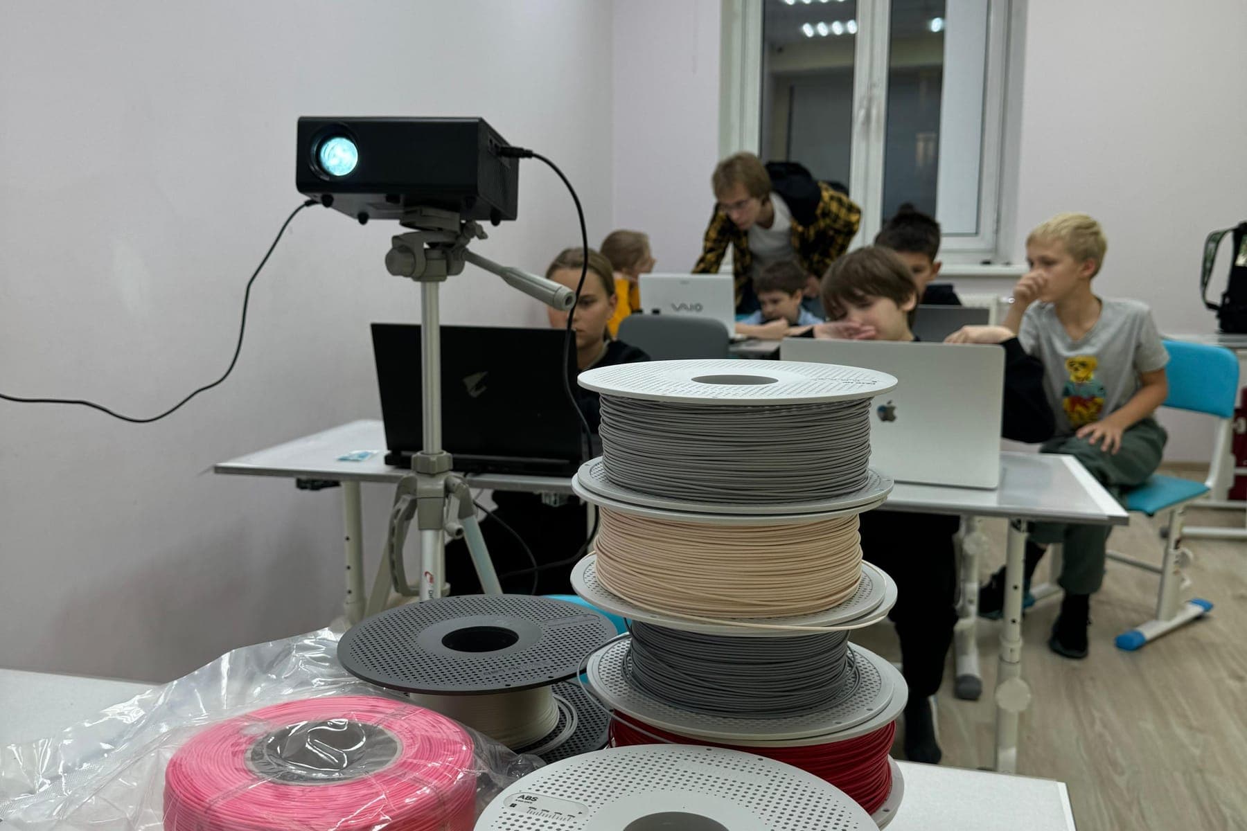 Катушки пластика для 3D-печати, за ними дети за ноутбуками