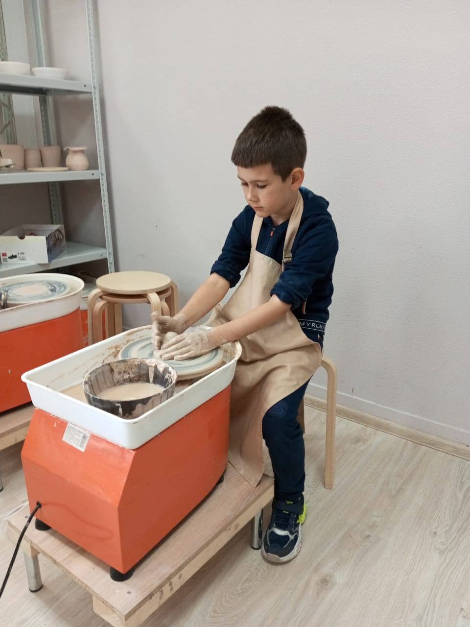 Мальчик в фартуке работает с глиной на гончарном круге