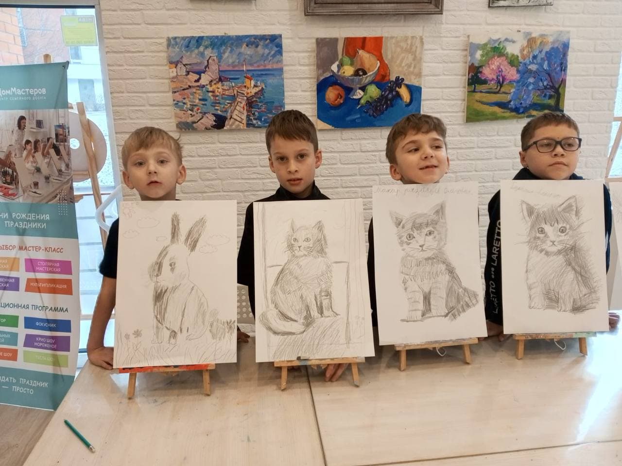 Четверо мальчиков показывают свои рисунки на мольбертах